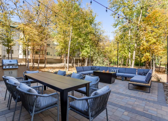 a patio with couches tables and chairs and trees at Birchwood Apartment Homes in Maple Grove, MN