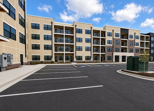 Apartments in Kokomo, IN, with In-Unit Washer and Dryer - The Elwood Apartments - A Spacious Parking Lot, Beige Facade, Large Windows, And A Bright Blue Sky With Clouds.