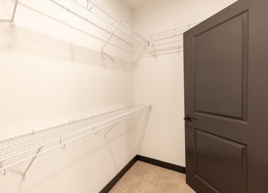 a walk in closet with white metal shelves and a black door