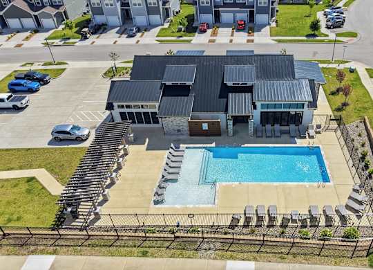 A swimming pool is surrounded by a fence and chairs in front of a building.