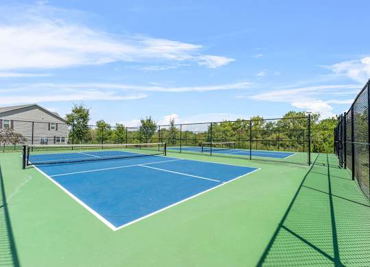 A tennis court with a blue surface and white lines, surrounded by a green fence.