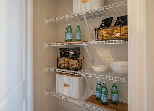 A white pantry with shelves stocked with food and drinks.