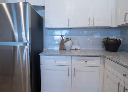 A kitchen with a stainless steel refrigerator and white cabinets.