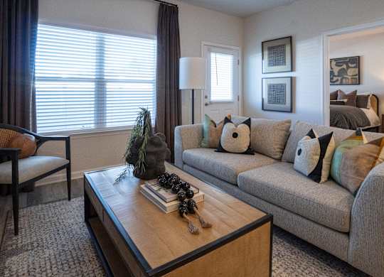 A living room with a grey couch, a brown chair, and a coffee table with a plant and a book on it.