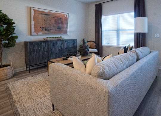 A living room with a grey couch and a painting on the wall.