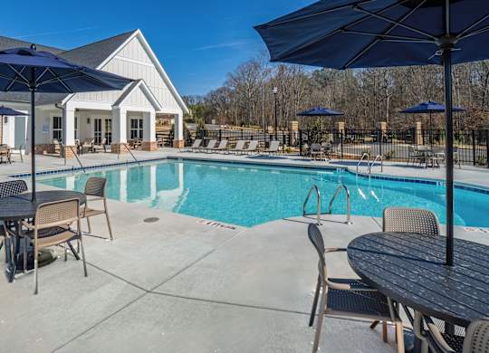 A pool area with a table and chairs and umbrellas.