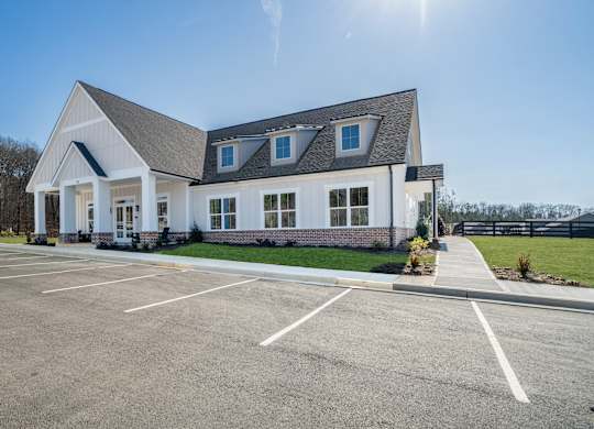 A white building with a grey roof and a parking lot in front.