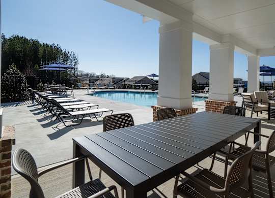 A table and chairs are set up on a patio with a pool in the background.