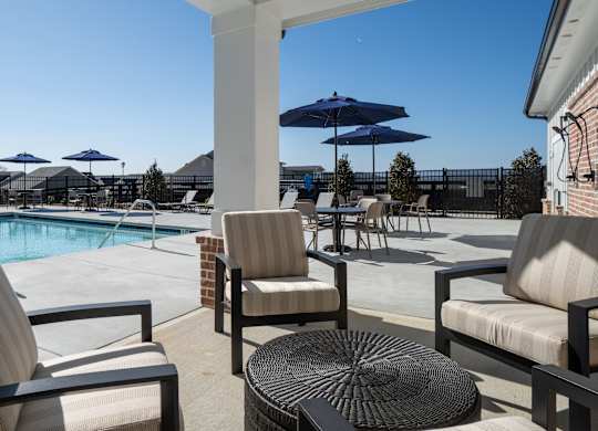 A patio with chairs and a table overlooks a pool.