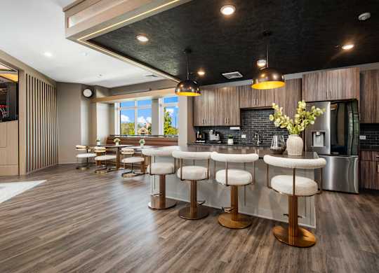 A modern kitchen with a bar area featuring white stools and a wooden floor.