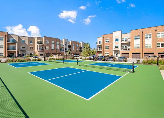 A tennis court is surrounded by apartment buildings.