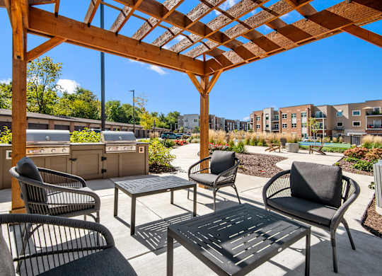 A wooden pergola with a table and chairs in front of a building.