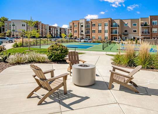A sunny day at a poolside with chairs and a fire pit.