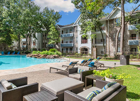 A pool surrounded by chairs and trees with apartment buildings in the background.