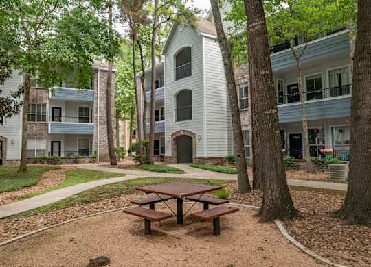 A picnic table sits in the middle of a dirt area with a building in the background.
