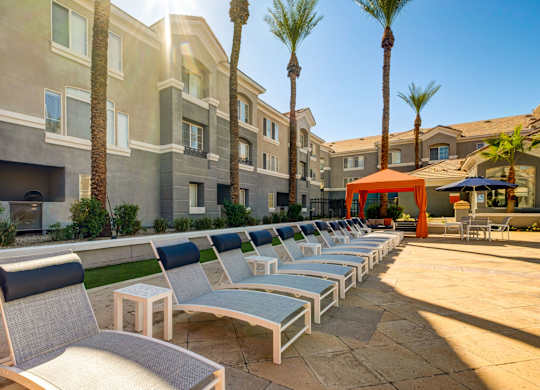A row of lounge chairs are set up on a patio in front of a building.