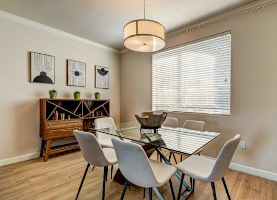 A dining room with a glass table and white chairs.