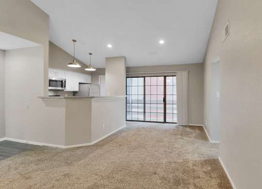 A spacious living room with a kitchen area and a large window.