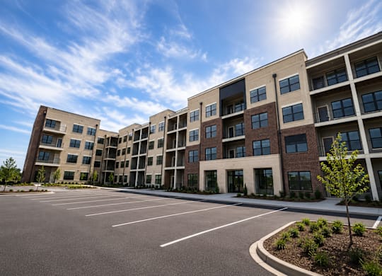 A sunny day at a modern apartment complex with a parking lot in front.