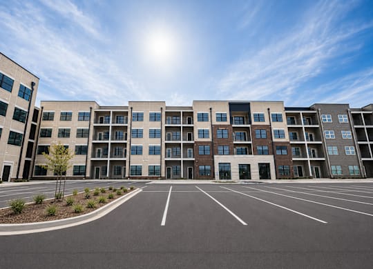 A sunny day at a modern apartment complex with a parking lot in front.