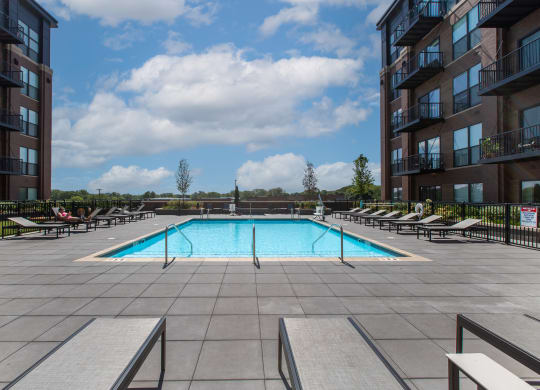 Maple Street Lofts - Big Pool with Deck, and Lounge Chairs, Surrounded by Apartment Building.