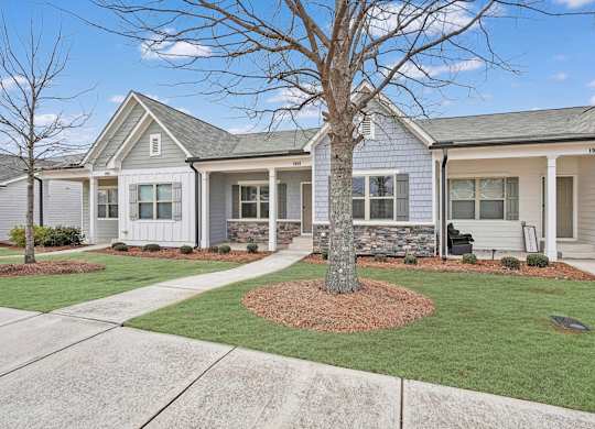 A house with a grey roof and white walls with a tree in front.