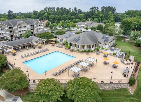 A large swimming pool surrounded by sun loungers and umbrellas in a resort-like setting.