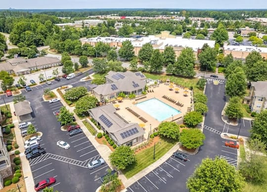 A bird's eye view of a parking lot with a swimming pool and buildings in the background.