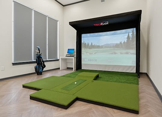 A room with a golf simulator and a golf bag.
