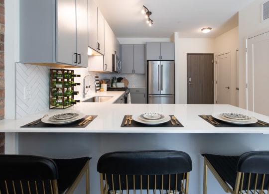 Maple Street Lofts - Kitchen With Light Grey Cabinets, Appliances, Track Lighting, and Breakfast Bar.
