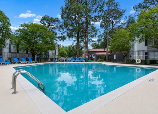 A swimming pool surrounded by trees and chairs.