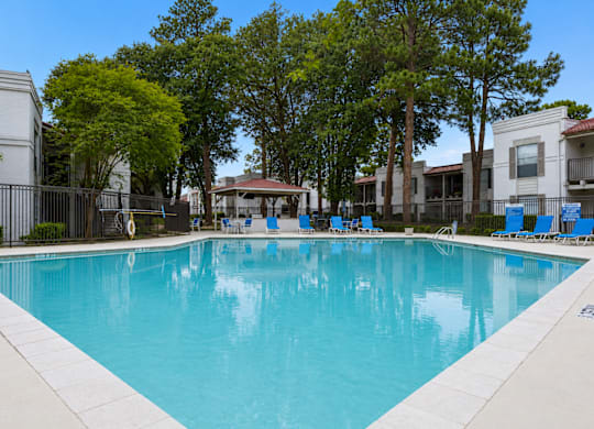 A large swimming pool surrounded by trees and chairs.