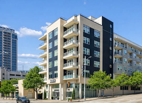 A modern apartment building with balconies and a car parked in front.