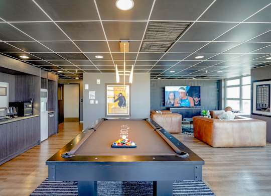 A pool table is in the middle of a room with a bar and a couch.