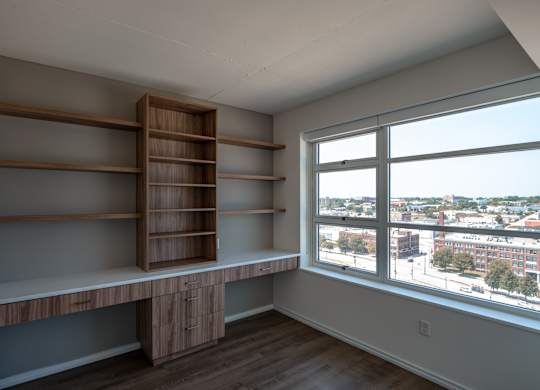 A room with a window overlooking a cityscape and a shelving unit.