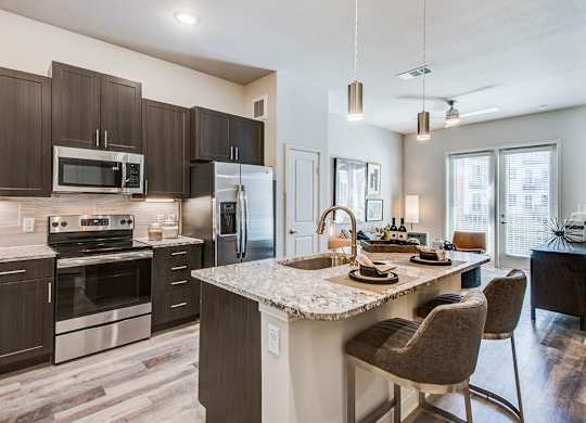Granite counter tops, stainless appliance package, medium brown cabinets, plank wood-style flooring, island seating, abundant cabinet and pantry space