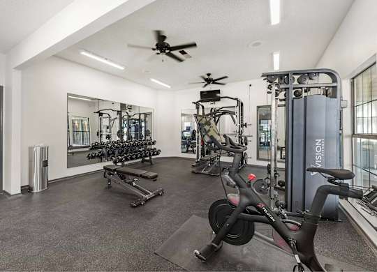 A gym with a variety of equipment including a stationary bike, a treadmill, and a rowing machine.