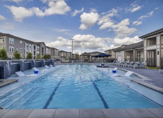 an outdoor pool with lounge chairs and buildings around it