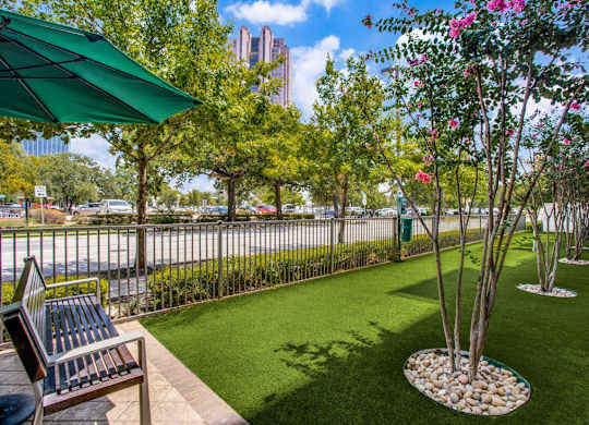 A green umbrella is on a bench in a landscaped yard.