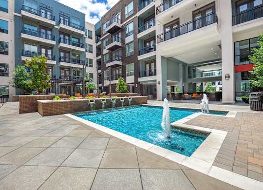 A large pool with a fountain in the middle of a courtyard surrounded by buildings.