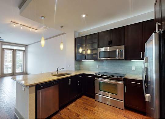 A modern kitchen with dark wood floors and stainless steel appliances.