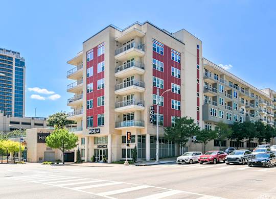 A red and beige apartment building with cars parked in front.