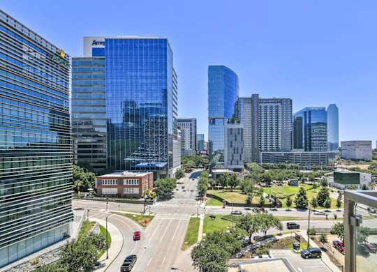 A cityscape with a mix of modern and older buildings, a clear blue sky, and a road with vehicles.
