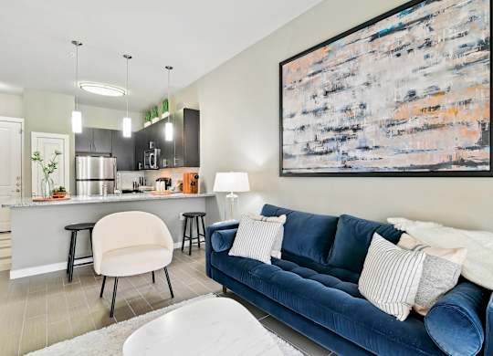 A blue couch with a white pillow is in the foreground of a modern kitchen and living room.