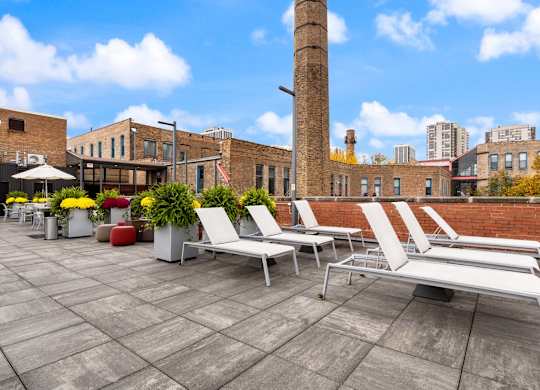 A patio with white chairs and a brick building in the background.
