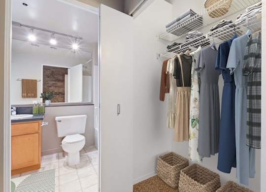 A white bathroom with a toilet and a white closet with clothes hanging.