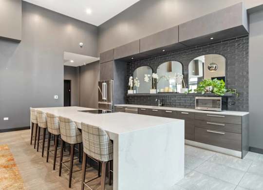 A modern kitchen with a long white island and dark wood floors.