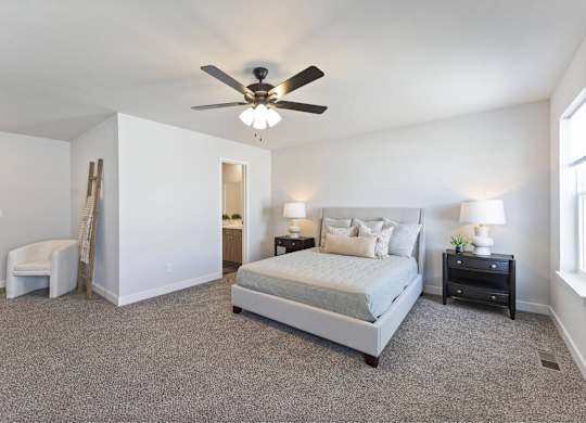 A bedroom with a large bed, a chair, and a ceiling fan.