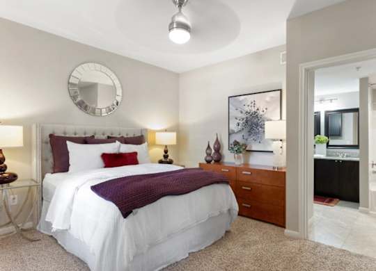 A bedroom with a white bed and a round mirror on the wall.