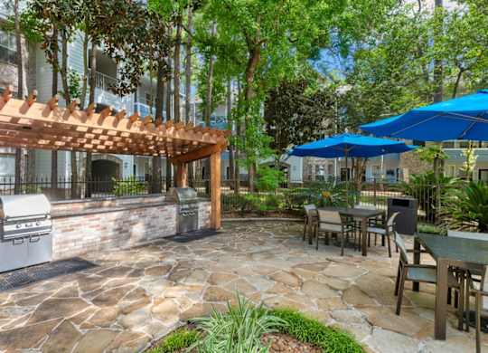A patio with a grill and a table under a blue umbrella.